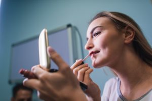 Young woman applying lipstick looking at mirror